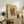 May include: Framed abstract art print with colorful geometric shapes in blues, reds, yellows and greens on beige background, displayed on rustic wooden sideboard alongside fern plant, ceramic vase, and stacked books in warm neutral living room setting with cream upholstered furniture