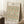 May include: A framed botanical print featuring William Morris's daisy pattern with green leaves, orange and coral flowers on cream background, displayed leaning against white wall corner on textured white rug. A coffee cup sits on wooden block nearby, with beige fabric visible at right edge.