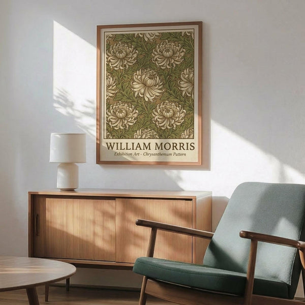 May include: Framed botanical art print featuring green and cream chrysanthemum floral pattern hanging on white wall above wooden sideboard. Mid-century modern living room with sage green upholstered armchair, round wood coffee table, and white ceramic table lamp. Natural sunlight creates geometric shadows across the minimalist Scandinavian-style interior.