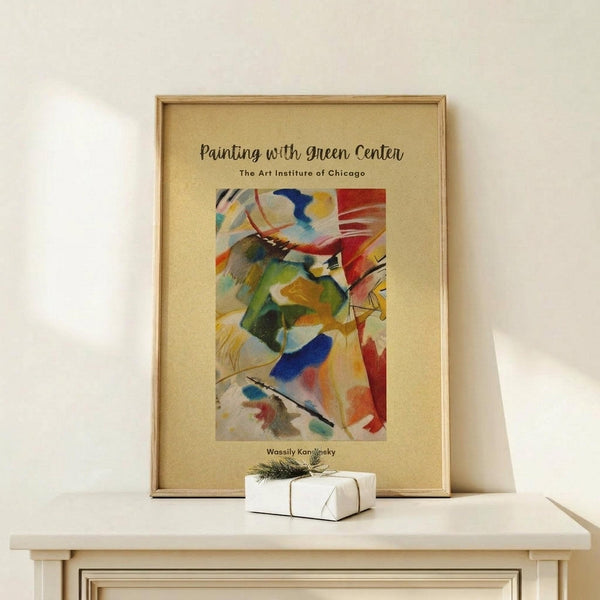 May include: Framed abstract art poster in light wood frame leaning against white wall on natural wood shelf. Artwork features vibrant colors including green, blue, red, yellow and orange in flowing brushstroke style. Small white wrapped gift box with evergreen sprig sits on shelf beside frame. Warm, minimal home decor setting with soft natural lighting.