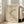 May include: Framed minimalist art print with abstract black curved lines on beige background, displayed in bright living room corner next to beige sectional sofa. White wooden frame leans against white wall with tall windows casting natural light shadows. Hardwood flooring visible beneath cream area rug.