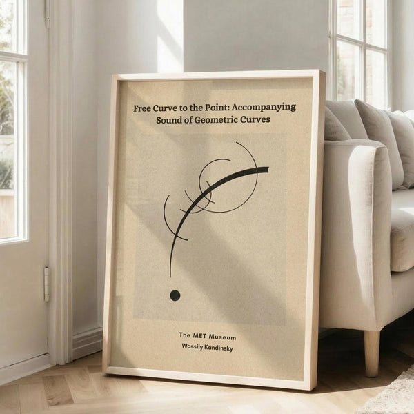 May include: Framed minimalist art print with abstract black curved lines on beige background, displayed in bright living room corner next to beige sectional sofa. White wooden frame leans against white wall with tall windows casting natural light shadows. Hardwood flooring visible beneath cream area rug.