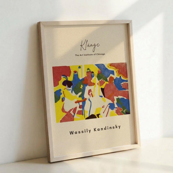 May include: Framed art print featuring Wassily Kandinsky's colorful abstract composition with bold shapes in red, yellow, blue, and green. The artwork shows flowing, organic forms and figures rendered in vibrant primary colors. Text reads "Klänge" and "The Art Institute of Chicago" above the image, with "Wassily Kandinsky" below. Natural wood frame displayed against white wall, leaning on surface with soft natural lighting creating gentle shadows.