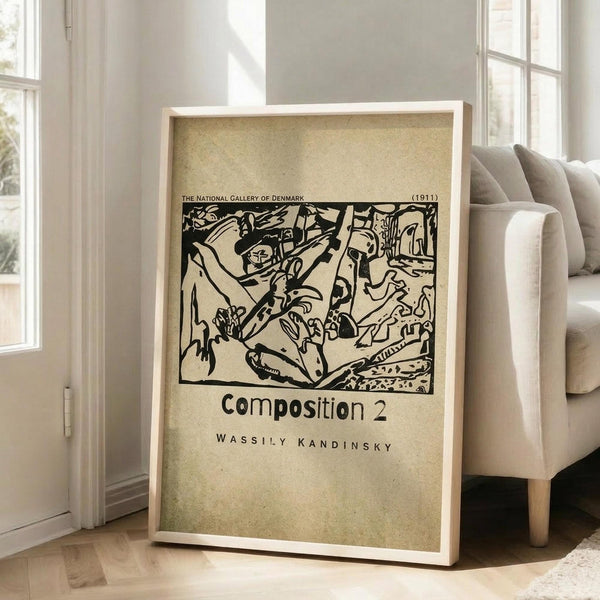 May include: Framed art print leaning against white wall next to beige armchair in bright living room. Print features black abstract linear artwork on cream background with museum-style text layout. Natural wood frame, approximately 2 feet tall, sits on light wooden floors with white baseboards and large windows visible.