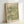 May include: Framed vintage-style botanical poster with sage green and cream floral pattern featuring detailed flowers and leaves. Light wood frame displayed against white wall, showing William Morris Gallery exhibition text from August 1887 with quote about art and materials at bottom.