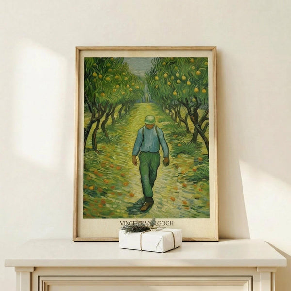 May include: Van Gogh poster print in light wood frame showing figure in blue shirt and green pants walking through orchard with yellow fruit trees. Framed artwork leans against white wall on pale wood console table next to small white wrapped gift with twine and greenery sprig.