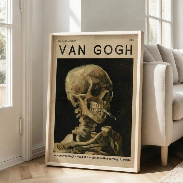 May include: Framed Van Gogh museum poster featuring skeleton with cigarette painting, displayed on light wooden floor against white wall next to beige upholstered chair. Print shows skull and ribcage in warm yellows and browns against dark background, with museum text and 1886 date. Natural sunlight streams through tall windows creating soft shadows on hardwood flooring.