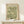May include: Framed vintage botanical poster featuring William Morris floral pattern in sage green and cream tones, displayed on light wood console table beside small white gift box with dried sprig, against neutral wall background.