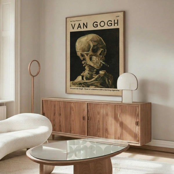 May include: Van Gogh museum poster of skull with cigarette artwork displayed above walnut wood credenza in minimalist living room with white curved chair, glass coffee table, and modern lamp. Poster shows skeleton head with burning cigarette against dark background in vintage exhibition style with cream border.