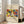 May include: A framed art poster leaning against a white wall next to a beige upholstered chair. The poster features a vibrant abstract artwork with bold colors including red, yellow, blue, green, and orange in flowing, organic shapes. The piece has handwritten-style text at the top and bottom on a cream background. Natural sunlight streams through nearby windows onto light wooden floors, creating a bright, modern living room setting.