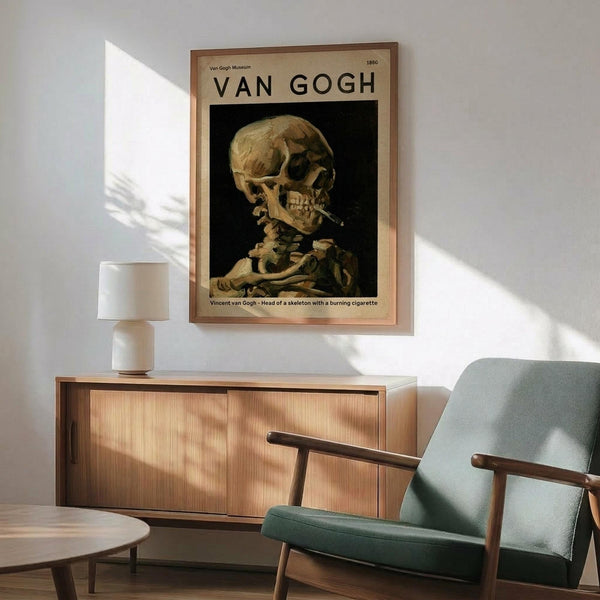 May include: Van Gogh museum poster of skeleton smoking cigarette hanging on white wall above wooden credenza. Mid-century modern living room with sage green armchair, white table lamp, and natural sunlight casting shadows. Poster shows yellowed skull against dark background in vintage-style frame.