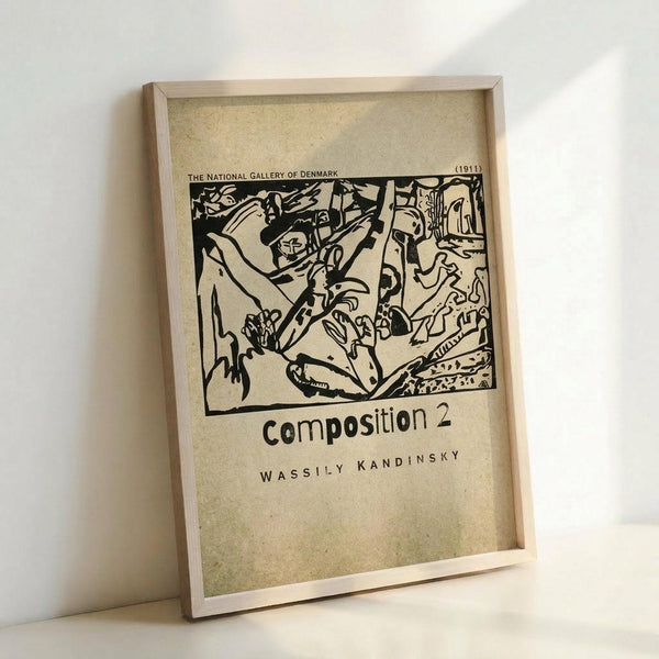 May include: Framed vintage-style poster featuring Wassily Kandinsky's abstract black and white artwork from 1911. The print shows bold, flowing organic shapes and lines in an expressionist style, with text identifying it as "Composition 2" and "The National Gallery of Denmark." The beige-toned poster is displayed in a simple light wood frame, leaning against a white wall on what appears to be a light surface.