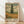 May include: Framed art print featuring a tall dark cypress tree in a golden wheat field under swirling cloudy sky, displayed in light wood frame against white textured wall on wooden floor. Print shows Van Gogh's characteristic bold brushstrokes and earthy color palette of greens, golds, and cream tones with French text at bottom.
