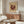 May include: Framed museum poster featuring abstract geometric design in burgundy on cream background, displayed above mid-century walnut credenza in modern living room with white curved chair, glass coffee table, and minimalist decor