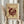 May include: Person in cream sweater holding framed abstract art poster featuring burgundy geometric circles, lines and dots on beige background, displayed in light wood frame against white curtained window, with dried wheat stems held in other hand