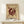 May include: Framed abstract art poster with burgundy geometric design on cream background, displayed on light wood surface next to small wrapped gift. Features circular forms with radiating lines in modernist style. Wooden frame with glass, leaning against white wall in minimalist interior setting.