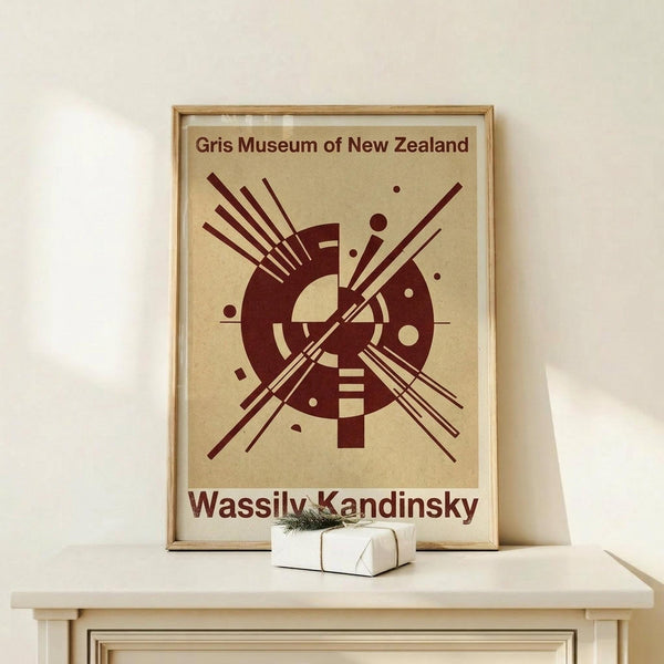 May include: Framed abstract art poster with burgundy geometric design on cream background, displayed on light wood surface next to small wrapped gift. Features circular forms with radiating lines in modernist style. Wooden frame with glass, leaning against white wall in minimalist interior setting.