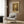May include: Vintage-style poster featuring brown bear in forest setting with "Preserve Nature" message, displayed on wood-paneled wall above cream upholstered chair with geometric pillow. Modern brass floor lamp and side table with open book complete the warm, neutral-toned reading nook scene.