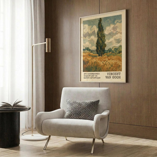 May include: Van Gogh-inspired poster featuring a tall dark cypress tree in a golden wheat field under swirling cloudy sky, displayed in light wood frame on warm brown wood-paneled wall above beige upholstered armchair with geometric patterned pillow, beside brass floor lamp and dark round side table with open book