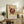 May include: Framed abstract art print with burgundy geometric design featuring radiating lines and circular elements on cream background, displayed on rustic wooden sideboard with books, ceramic vase, and fern plant in cozy living room setting with beige armchair and neutral walls