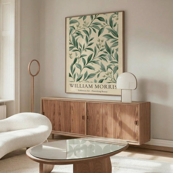 May include: Framed botanical poster with green leafy pattern on cream background displayed above wood sideboard in modern living room. Room features white curved chair, glass oval coffee table, brass floor lamp, and neutral walls with natural lighting.