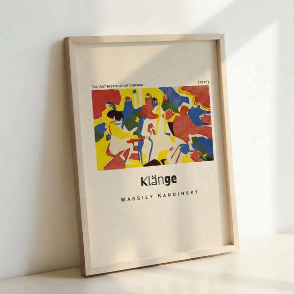May include: Framed museum exhibition poster featuring Wassily Kandinsky's abstract artwork in vibrant primary colors - red, blue, yellow with geometric and organic shapes. The colorful composition shows dynamic movement with various forms and figures. Text reads "The Art Institute of Chicago (1913)" at top, "Klänge" and "Wassily Kandinsky" below the artwork. Light wood frame with white matting, leaning against white wall corner.