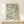 May include: A framed botanical art print featuring flowing green leaves and stems in William Morris style on cream background, displayed on a light wood console table with a small wrapped gift box beside it against a neutral wall.