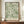 May include: Framed botanical poster with flowing green and cream foliage pattern on sage background, displayed on wooden sideboard next to white ceramic vase and stacked books. The artwork features swirling leaf motifs in William Morris style with text at bottom. Warm lighting illuminates the cream-colored room with decorative wall molding.