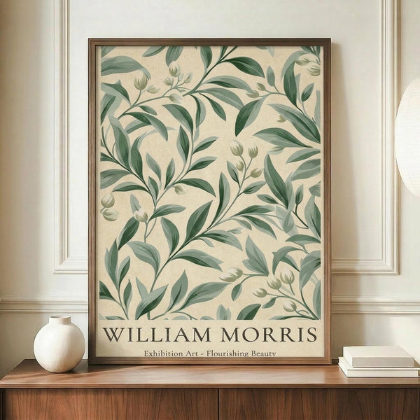 May include: Framed botanical art print with green leafy pattern on cream background, displayed on wooden sideboard next to white ceramic vase and stacked books. Features William Morris-style foliage design with flowing stems, leaves, and small buds in sage green tones. Print shown in thin brown frame against white paneled wall in elegant interior setting.