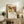 May include: Framed art print displayed on rustic wooden sideboard in living room setting. Abstract colorful artwork features bold red, blue, yellow shapes with geometric figures. Light wood frame with white matting. Scene includes cream upholstered chair, fern plant, stacked books, ceramic vase, and neutral wall background. Print shows vibrant modernist style with angular human forms and dynamic composition.