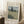 May include: Framed Van Gogh painting print leaning against white wall on textured cream rug. Artwork shows golden wheat field with tall dark cypress tree, rolling hills, and cloudy sky in post-impressionist style. Natural wood frame, displayed near wooden block with white coffee cup and beige blanket.