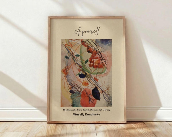 May include: Framed abstract watercolor artwork in wooden frame leaning against white wall on light wood floor. The painting features flowing organic shapes in red, orange, green, and blue with dynamic black lines and curves. Cream matting surrounds the colorful contemporary art piece. Natural lighting creates soft shadows across the minimal room setting.