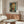 May include: Van Gogh self-portrait print in thin wooden frame hanging above walnut sideboard with glass oval coffee table and cream swivel chair in bright modern living room with white walls and natural lighting
