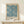 May include: A framed botanical poster featuring an intricate blue and cream floral pattern with marigold flowers and flowing foliage in William Morris's distinctive Arts and Crafts style. The print is displayed in a light wood frame on a cream-colored wooden console table against a neutral wall, with a small wrapped gift box placed in front.