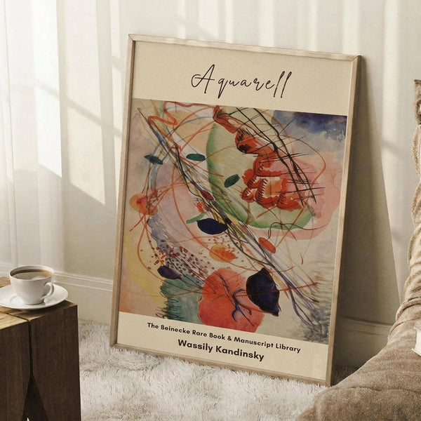 May include: Framed abstract watercolor art print with swirling brushstrokes in red, blue, green, and orange tones, leaning against white wall beside wooden side table with white coffee cup. The poster features flowing organic shapes and dynamic lines in Kandinsky's distinctive abstract style, displayed in light wooden frame on textured cream rug.