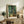 May include: Framed Van Gogh Cypresses print with swirling green and yellow brushstrokes depicting tall cypress trees, displayed on rustic wooden sideboard alongside fern plant, cream ceramic vase, stacked books, and brown leather armchair in warm neutral living room setting with natural lighting.