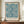 May include: Framed poster with blue botanical pattern featuring marigold flowers and flowing foliage on cream background, displayed on wooden credenza alongside white ceramic vase and stacked books against neutral wall with white molding
