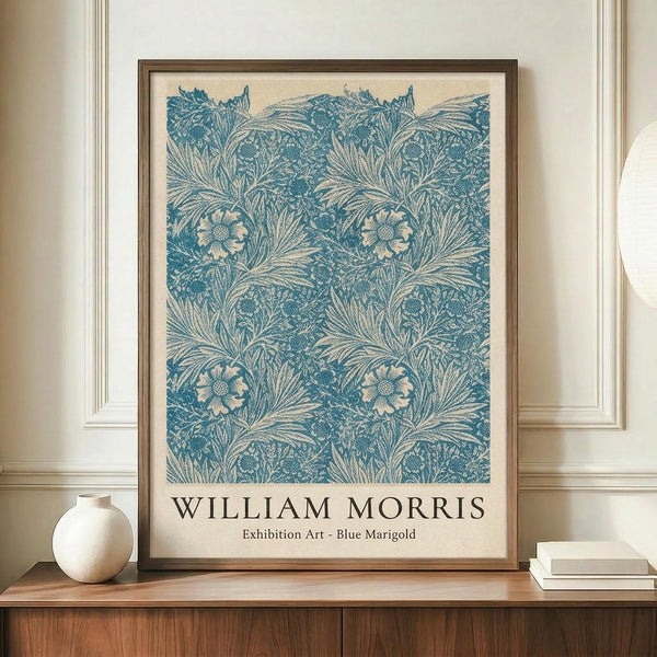 May include: Framed poster with blue botanical pattern featuring marigold flowers and flowing foliage on cream background, displayed on wooden credenza alongside white ceramic vase and stacked books against neutral wall with white molding