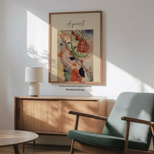 May include: Abstract watercolor artwork by Kandinsky displayed in thin wood frame on white wall above wooden sideboard. Painting features flowing organic shapes in orange, green, blue and black with curved lines and circular forms. Mid-century modern living room setting with sage green upholstered chair, white ceramic table lamp, and natural sunlight casting shadows across the scene.