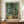 May include: Framed Van Gogh print featuring swirling cypress trees in vibrant greens and blues with characteristic flowing brushstrokes, displayed on wooden sideboard beside white ceramic vase and stacked books in elegant room with cream walls and wainscoting