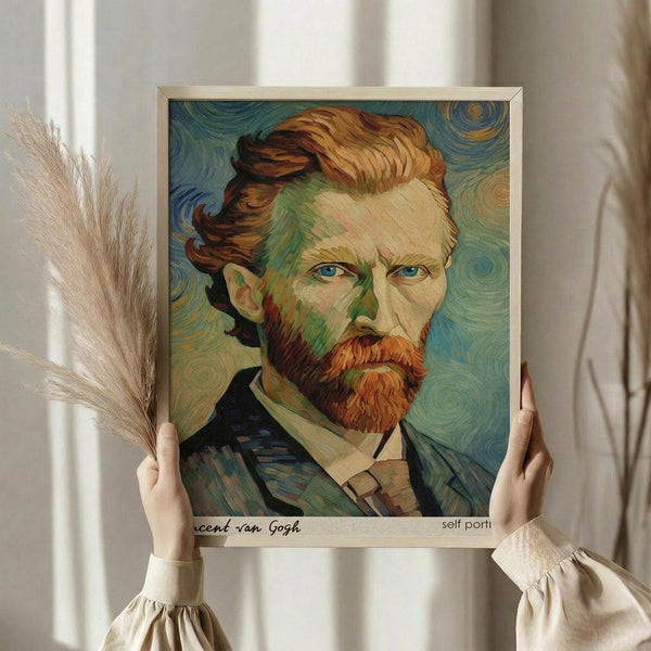 May include: Person holding framed art print featuring Van Gogh's self-portrait with swirling blue and green background, reddish-brown hair and beard, shown in light wooden frame. Hands wear cream-colored ruffled sleeves, dried pampas grass visible on left side against soft white curtained background.