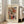 May include: Framed abstract art print leaning against white wall next to beige sofa in bright living room. Artwork features swirling watercolor forms in red, orange, green, and black with flowing lines and organic shapes. Light wooden frame with cream matting displays cursive script at top and attribution text below the colorful abstract composition.