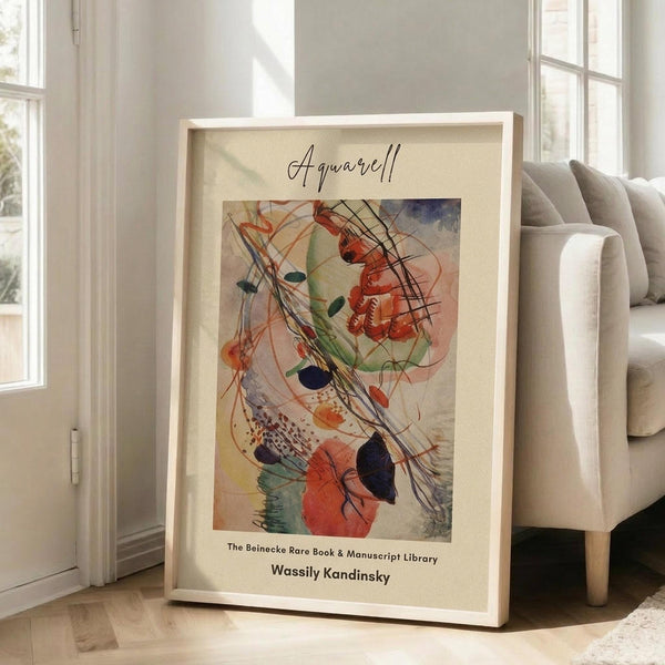 May include: Framed abstract art print leaning against white wall next to beige sofa in bright living room. Artwork features swirling watercolor forms in red, orange, green, and black with flowing lines and organic shapes. Light wooden frame with cream matting displays cursive script at top and attribution text below the colorful abstract composition.
