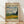 May include: Framed Van Gogh museum poster featuring "Wheat Field with Cypresses" painting with swirling blue and white clouds, golden wheat field, and dark cypress trees. Beige background with black text and 1889 date. Natural wood frame leaning against white wall on light wooden floor with soft window shadows.