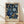 May include: Framed botanical art print with intricate blue and cream floral pattern on dark background, featuring ornate blooming flowers and decorative foliage in William Morris style. Light wood frame sits against white wall on natural hardwood floor with soft window light creating shadows.