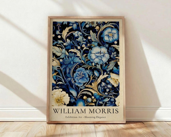 May include: Framed botanical art print with intricate blue and cream floral pattern on dark background, featuring ornate blooming flowers and decorative foliage in William Morris style. Light wood frame sits against white wall on natural hardwood floor with soft window light creating shadows.