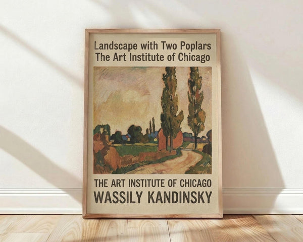 May include: Framed poster of Kandinsky's landscape painting featuring two tall poplar trees, winding path, and buildings in earthy tones of green, brown, and orange. Art Institute of Chicago exhibition poster in light wood frame, leaning against white wall on light wooden floor with natural shadows.
