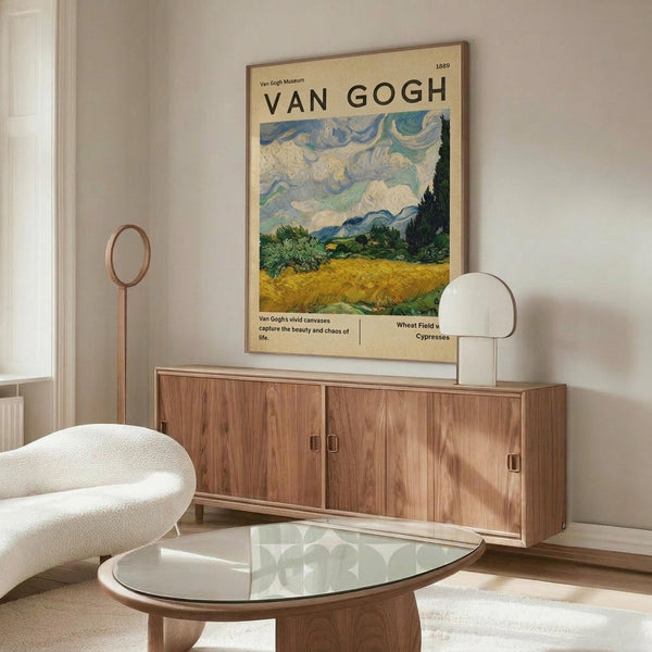May include: Van Gogh museum poster featuring Wheat Field with Cypresses painting displayed above wooden credenza in modern living room. Poster shows swirling blue sky, golden wheat field, and dark cypress tree. White sculptural chair and glass coffee table visible. Warm wood tones throughout minimalist space with cream walls.