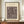 May include: Framed museum poster with abstract geometric shapes and lines in brown tones on cream background, displayed on wooden sideboard next to white ceramic vase and stacked books in elegant room with white wainscoting and beige walls