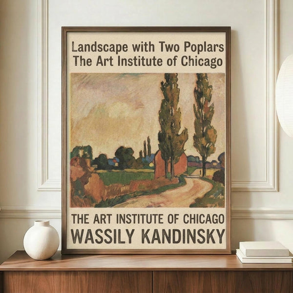 May include: Framed vintage museum exhibition poster featuring Wassily Kandinsky's colorful landscape painting with two prominent poplar trees, red buildings, and winding path under peachy sky. Displayed on wooden sideboard next to white ceramic vase and stacked books in elegant room with cream walls and white molding.